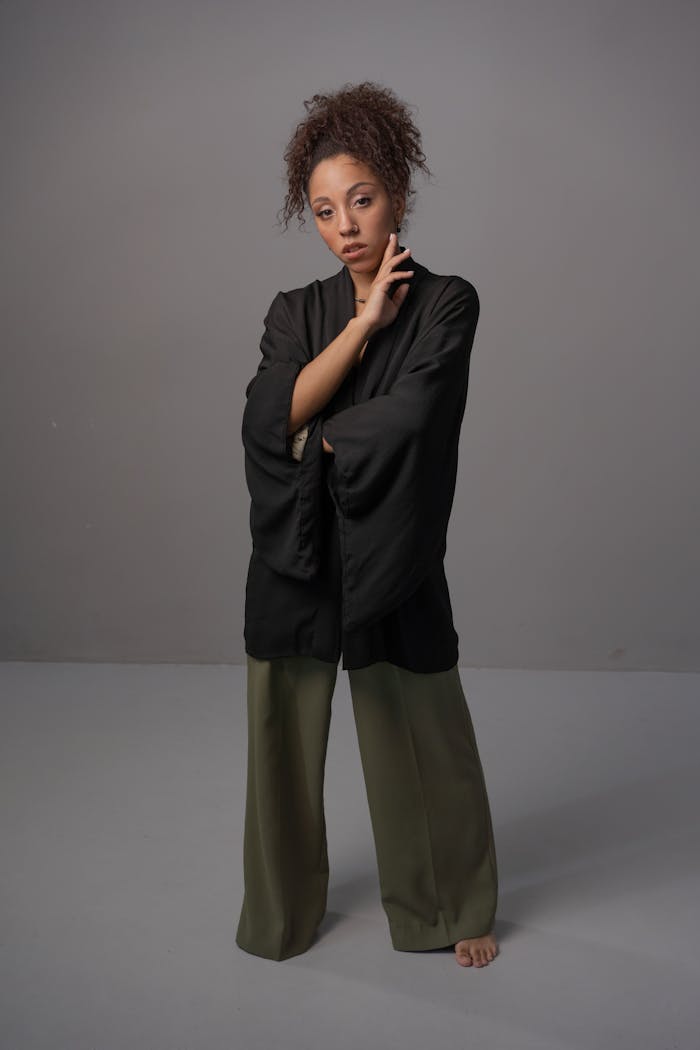 Studio portrait of a young adult woman in a chic black kimono and green pants against a neutral background.